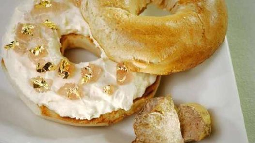 Bagel s bílým krémovým sýrem, plátky lososa a lupínky jedlého zlata na bílém talíři