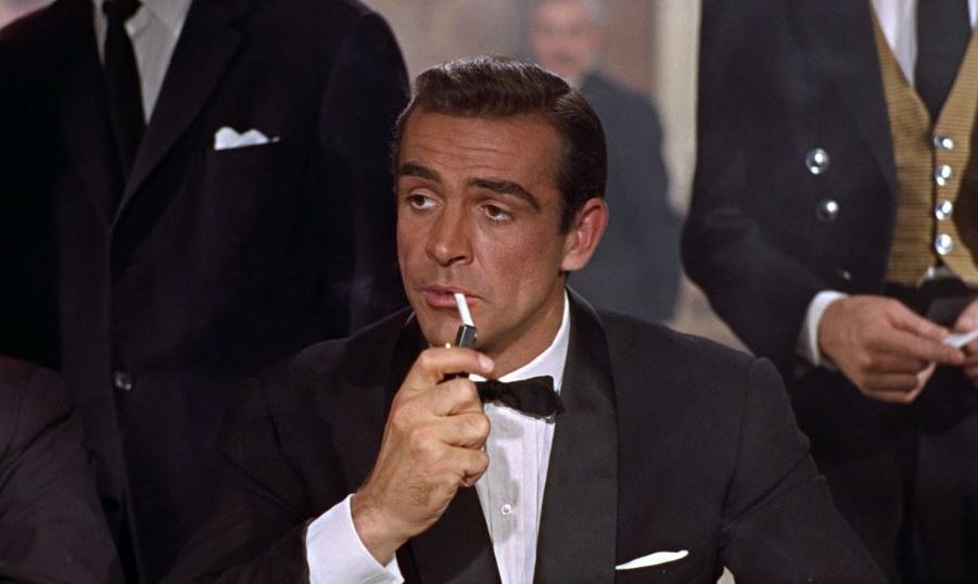 Sean Connery jako James Bond v černém smokingu si zapaluje cigaretu