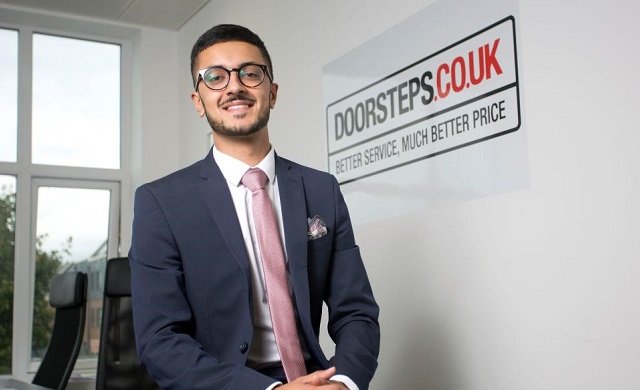 Mladý muž v obleku s brýlemi a růžovou kravatou před logem Doorsteps.co.uk s heslem "Better service, much better price"