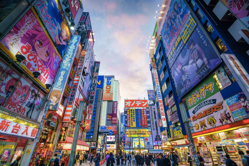 Různobarevné neonové reklamy a anime bannery na budovách v tokijské čtvrti Akihabara plné lidí