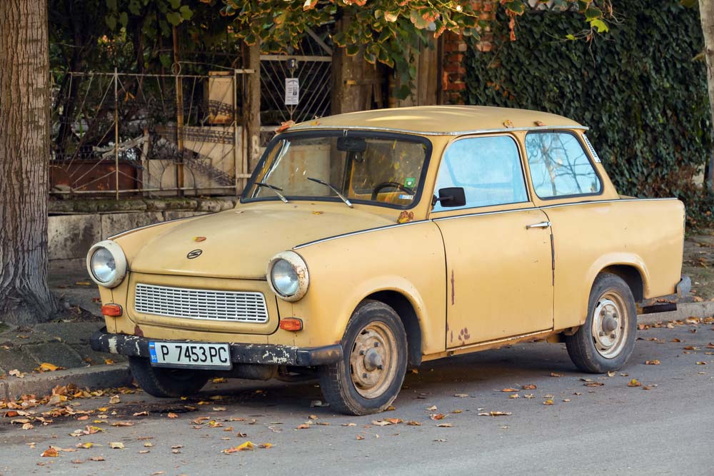 Béžový Trabant zaparkovaný u chodníku pod stromem s podzimním listím