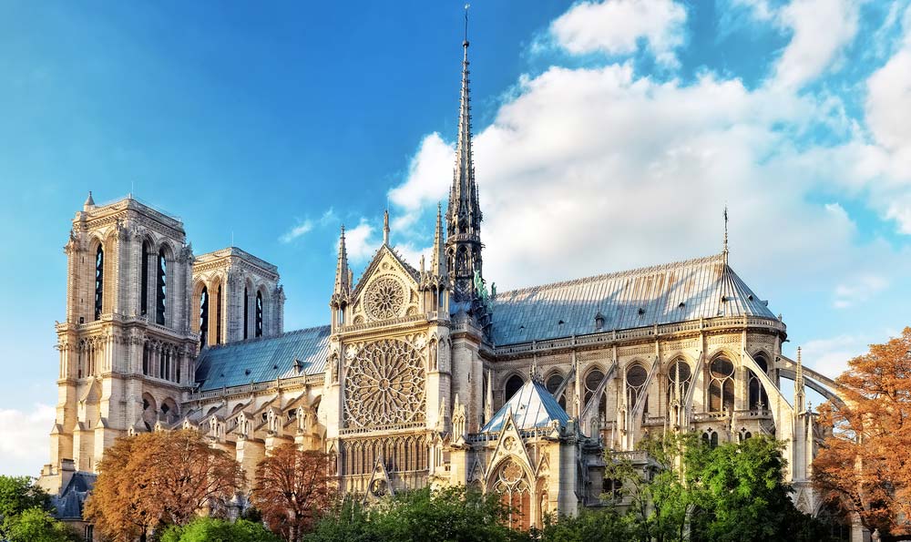 Katedrála Notre-Dame v Paříži s věžemi a štíhlou špičatou věžičkou na pozadí modré oblohy