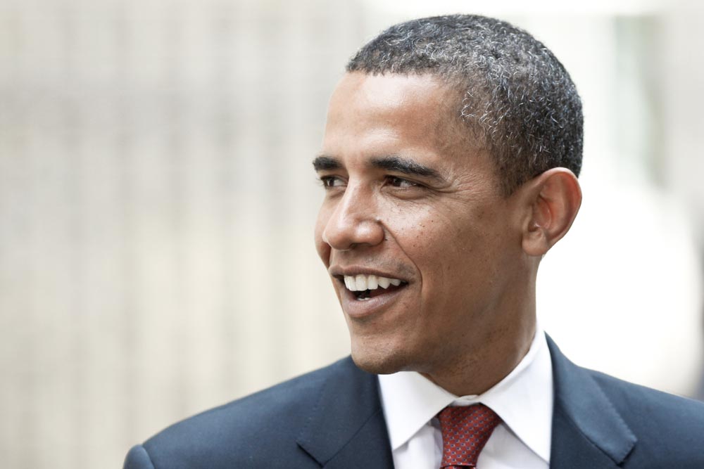 Barack Obama usmívající se z profilu, v tmavém obleku s červenou kravatou