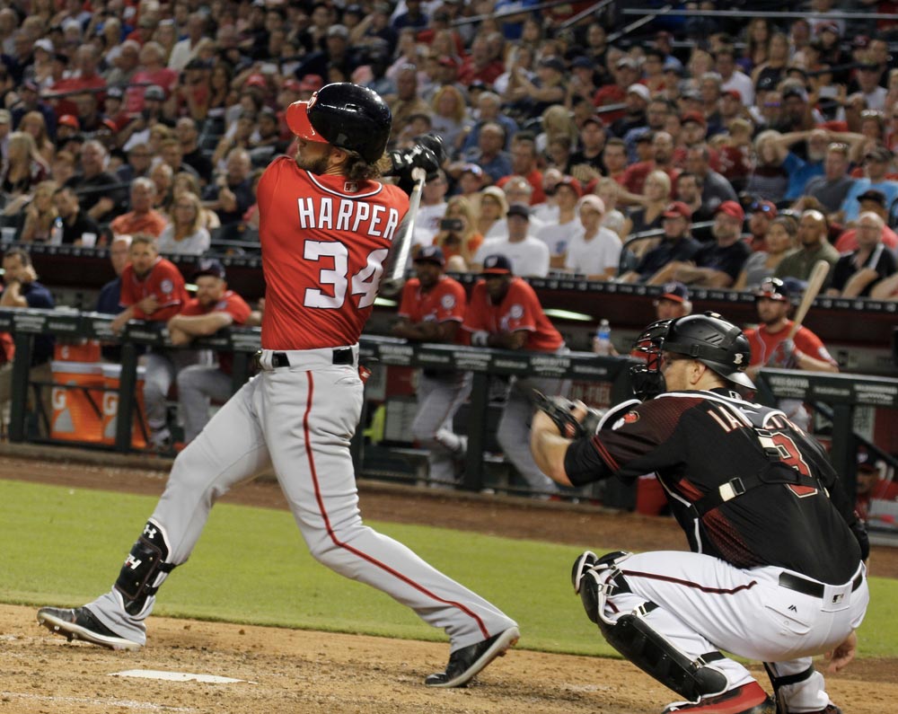 Baseballista Bryce Harper v dresu s číslem 34 při odpalu, za ním chytač