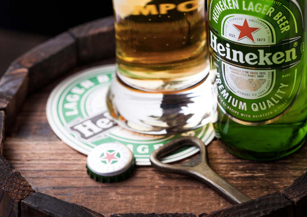 Láhev a sklenice piva Heineken s otvírákem a víčkem na dřevěném sudu