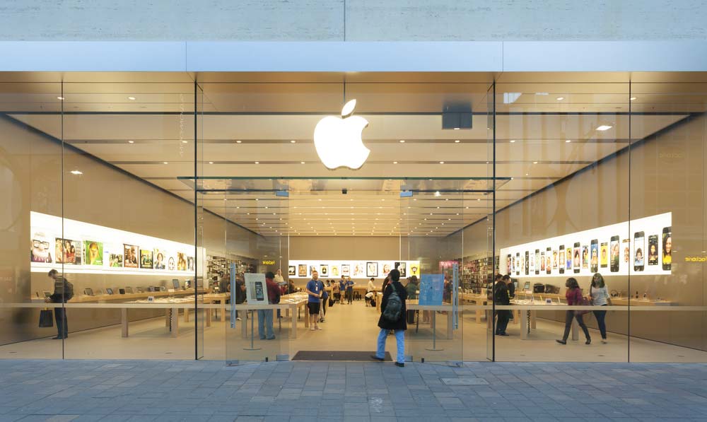 Prosklená fasáda obchodu Apple Store se svíceným logem jablka a zákazníky uvnitř