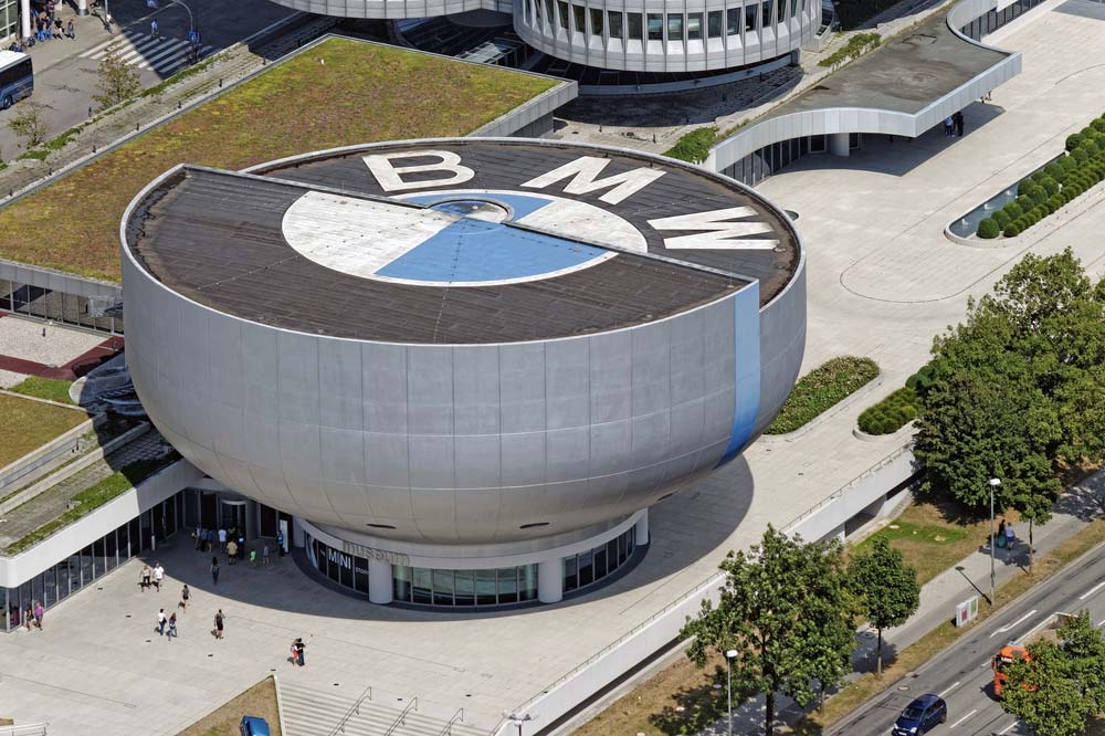 Budova muzea BMW ve tvaru mísy s velkým logem BMW na střeše, letecký pohled