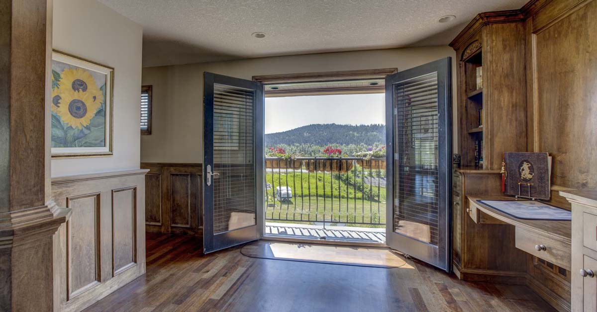Interiér domu s otevřenými francouzskými dveřmi na balkon s výhledem na hory, obraz slunečnic na stěně