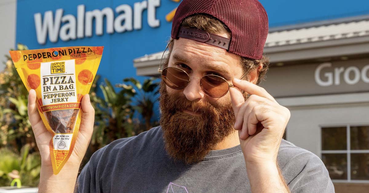 Vousaty muz v otocene kšiltovce a slunecnich brylich drzi balicek Pizza in a Bag pred prodejnou Walmart