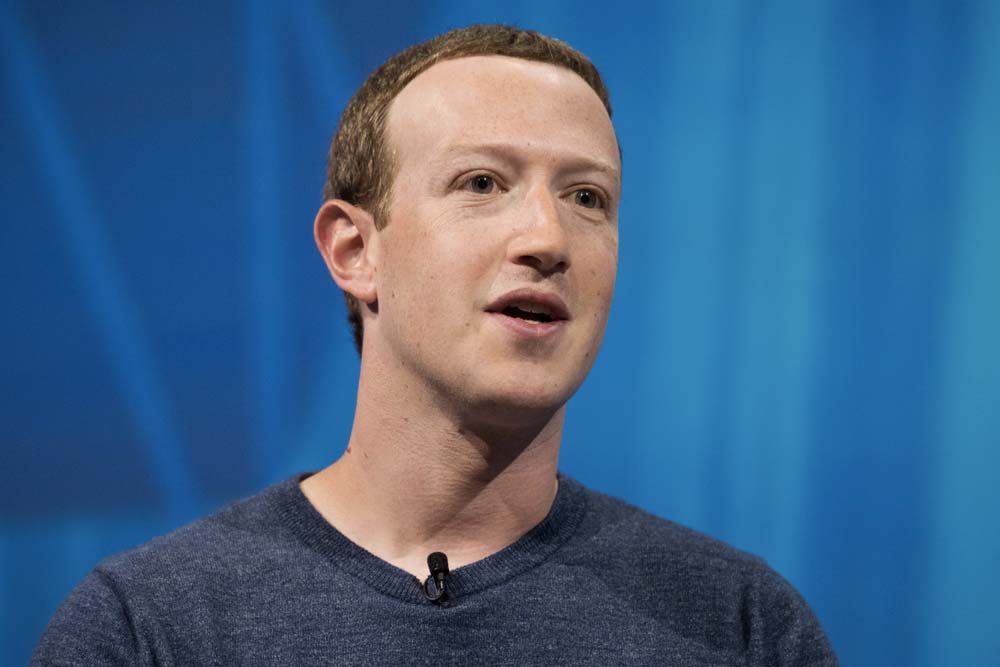 Mark Zuckerberg zblízka v šedém tričku při rozhovoru na modrém pozadí