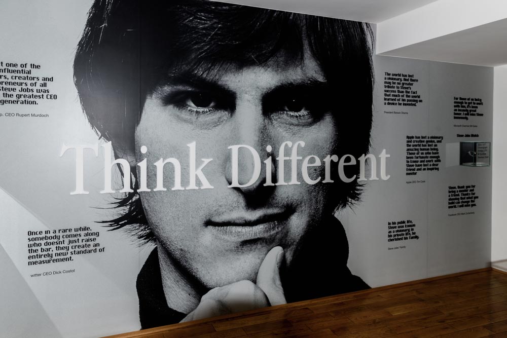 Černobílá nástěnná malba Steva Jobse s nápisem Think Different a citáty ředitelů firem jako Rupert Murdoch, Tim Cook nebo Mark Zuckerberg