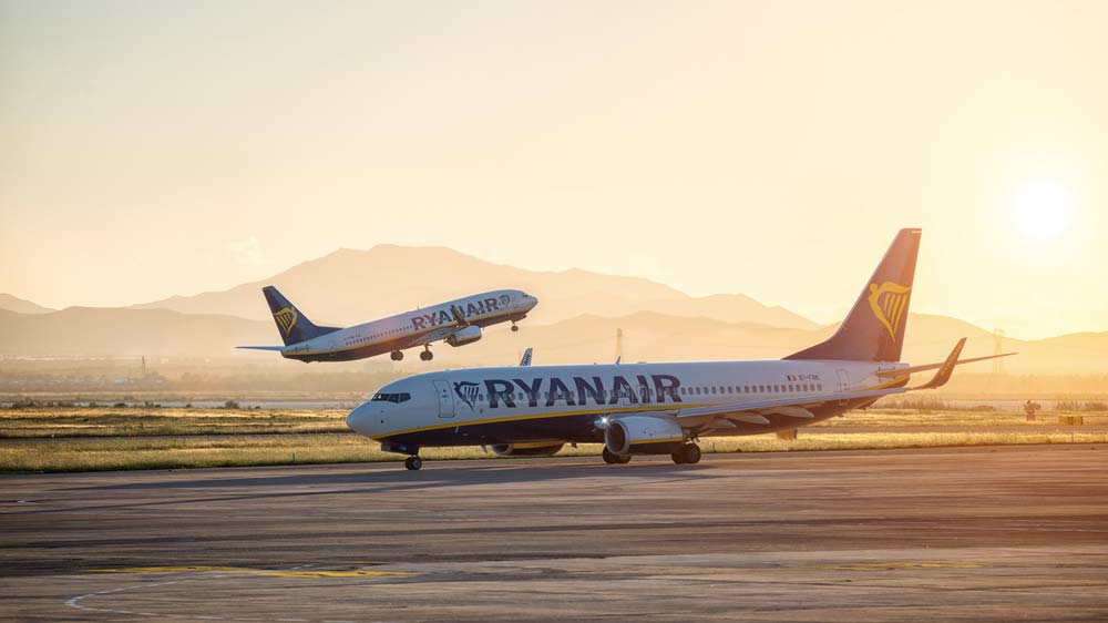 Dvě letadla Ryanair na ranveji - jedno vzlétá, druhé stojí na dráze při západu slunce