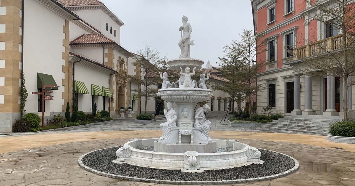 Kamenná fontána se sochou na náměstí obklopeném budovami ve stylu jihoevropského historického centra, s cedulí Granada