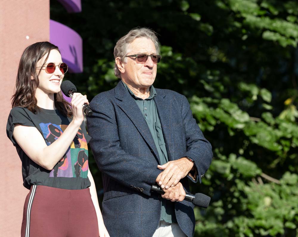 Herečka Rachel Brosnahan s mikrofonem vedle Roberta De Nira na venkovní akci