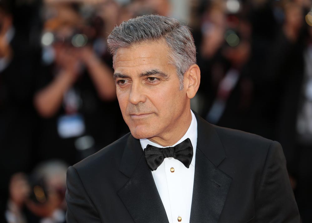 George Clooney ve smokingu s motýlkem na červeném koberci před fotografy