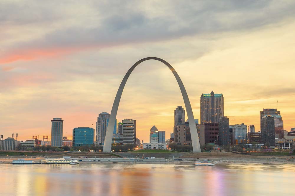 Gateway Arch v St. Louis nad řekou Mississippi s panoramatem města při západu slunce