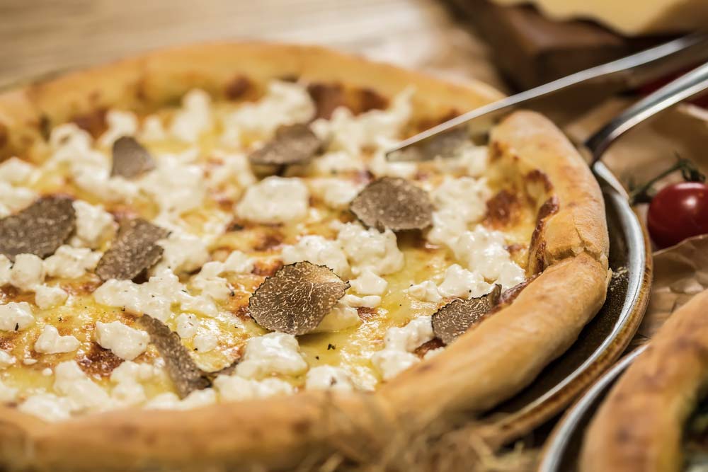 Pizza s bílými lanýži a mozzarellou, kleštěmi je odebírán jeden plátek