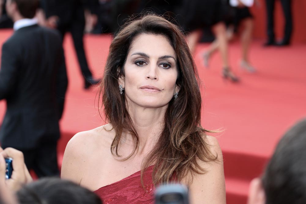 Cindy Crawford v červených šatech na červeném koberci, obklopena fotografy
