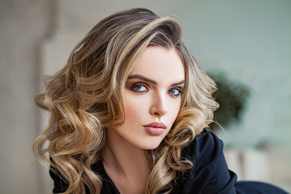 Žena s vlnitými vlasy melírovanými technikou balayage z tmavých kořínků do blond konečků