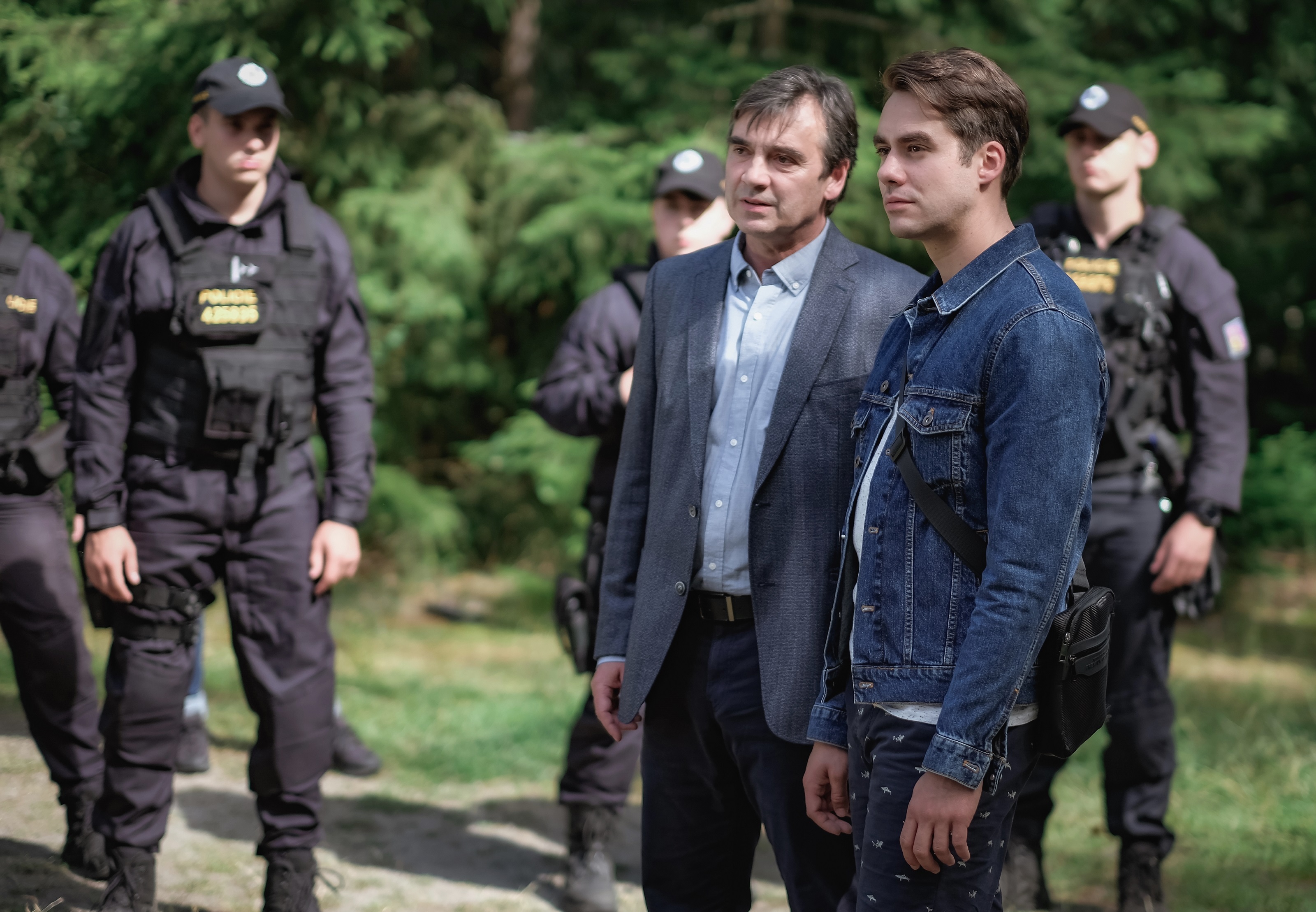 Herci ze seriálu Odznak Vysočina obklopení policisty v lesním exteriéru při natáčení