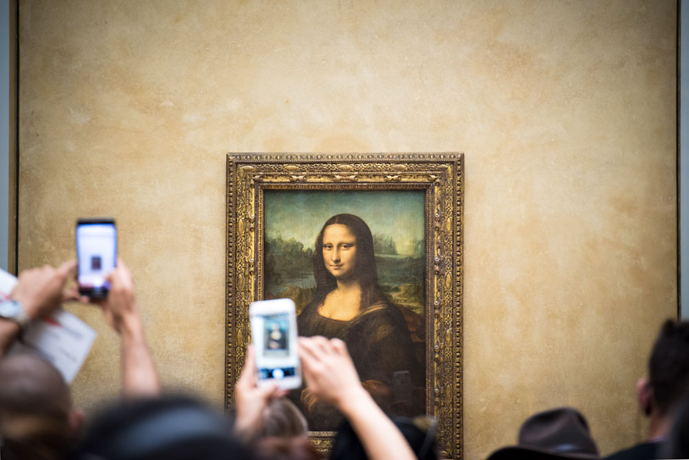 Obraz Mona Lisa v pařížské galerii Louvre. Míří na něj fotoaparáty mobilních telefonů, které patří návštěvníkům galerie.