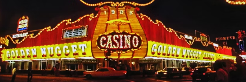 Nasvícený vchod kasina Golden Nugget v noci s neonovými nápisy Casino a Golden Nugget, auta zaparkovaná před vchodem